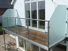 a balcony with glass railings and wooden flooring next to a white house on a sunny day