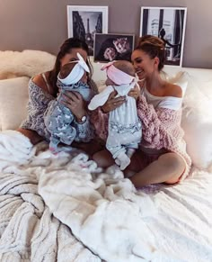 two women are sitting on a bed holding their babys and posing for the camera