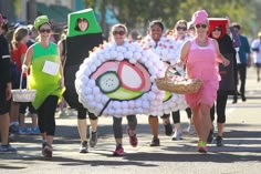 a group of people walking down the street in costumes and balloons on their heads as they run