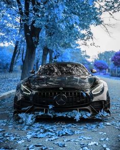 a black sports car parked on the side of a road with leaves all over it