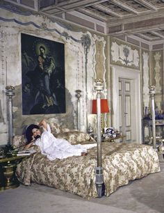 a woman in a white dress laying on a bed with a painting hanging above it