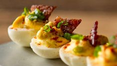 deviled eggs topped with bacon and green onions on a silver platter, ready to be eaten