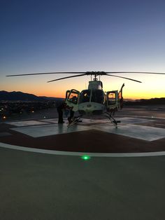 a helicopter sitting on top of an airport tarmac at sunset with the sun setting in the background