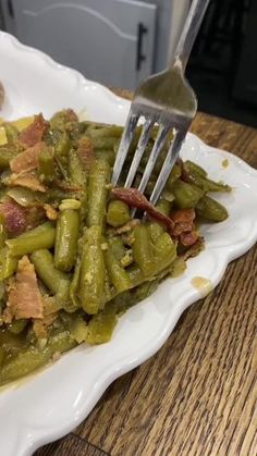 a white plate topped with green beans covered in bacon next to a knife and fork