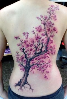 a woman's back with a tree tattoo on her left side and pink flowers in the center