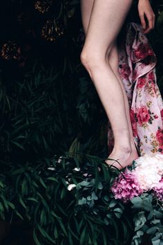 a woman standing on top of a lush green field next to flowers and leaves in front of her