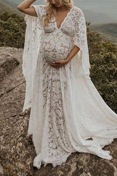 a pregnant woman standing on top of a rocky hill wearing a white dress and cape