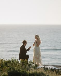 a man kneeling down next to a woman near the ocean