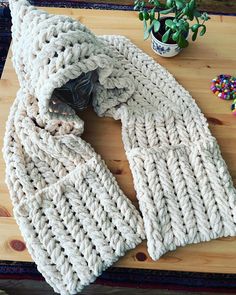 a knitted scarf sitting on top of a wooden table next to a potted plant