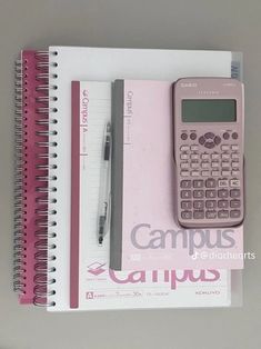 a pink calculator sitting on top of a spiral notebook next to a pen