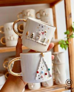 two coffee mugs with christmas decorations on them are being held by someone's hand