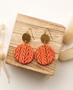 a pair of orange earrings with braided design on them sitting on top of a piece of wood