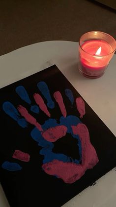 a lit candle sits on a table next to a handprint with red and blue ink