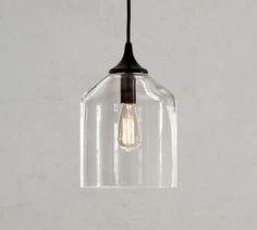 a clear glass light fixture hanging from a black metal ceiling hook on a white wall