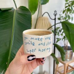 a person holding a coffee cup with writing on it in front of a potted plant