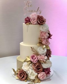 a three tiered wedding cake with pink and white flowers on the top, decorated with gold leaves