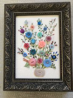 there is a framed picture with buttons and flowers in the frame on the wall behind it