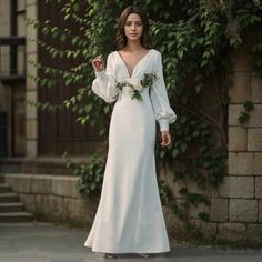 a woman in a white wedding dress standing on the street with greenery behind her