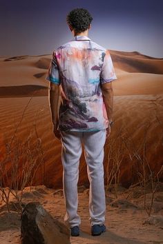 a man standing on top of a rock in the middle of a desert area with sand dunes behind him