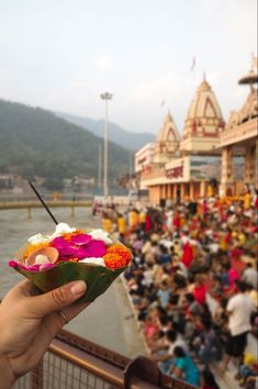 a person holding up a small bowl with flowers in front of a large group of people