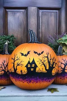 three pumpkins painted to look like halloween houses with bats and trees in the background