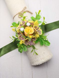 a boutonniere with yellow flowers and greenery tied to it on a white wooden surface