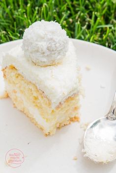 a piece of cake on a white plate with a silver spoon and green grass in the background