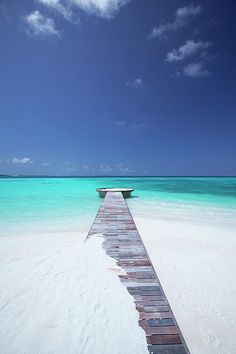 a long wooden dock extending into the ocean from a sandy beach with clear blue water