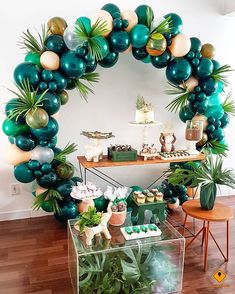 a table topped with lots of green and white balloons next to a wall filled with potted plants