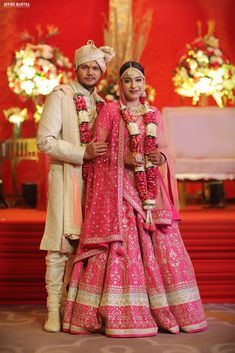 two people standing next to each other in front of a red wall and decorated with flowers