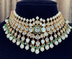 an elaborate necklace with pearls and emeralds on display in front of a black mannequin