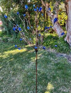 a metal tree with blue glass balls on it's branches in front of a house