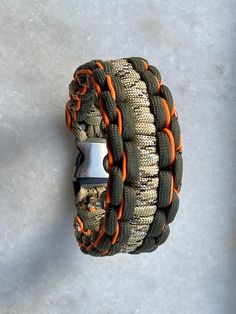 an orange and green bracelet with metal clasps on concrete floor next to white wall