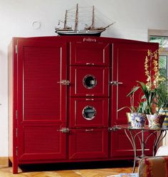 a red cabinet in the middle of a room with a boat on top of it