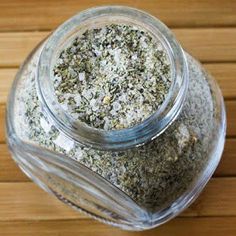 a glass jar filled with lots of different types of herbs on top of a wooden table