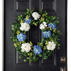 a wreath with blue and white flowers is hanging on the front door to welcome guests