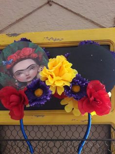 a yellow frame with some flowers and a picture on the top, in front of a chicken wire fence