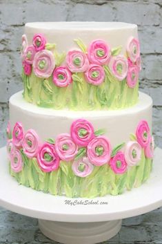 a three tiered cake decorated with pink and green icing flowers on a white pedestal