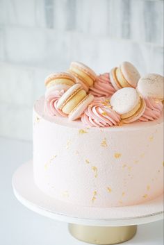 a pink and gold cake with macaroons on top sitting on a white table