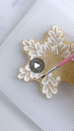 a cookie decorated like a snowflake with icing and a pink handled brush