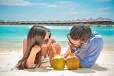 a man and woman laying on the beach with coconuts in front of their faces