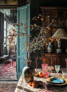 a dining room table with an orange tree in the center and vases on it