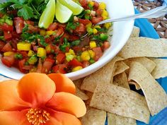 a white bowl filled with salsa next to tortilla chips and an orange flower