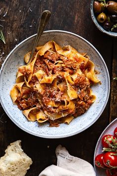 a bowl filled with pasta and meat on top of a wooden table next to bread