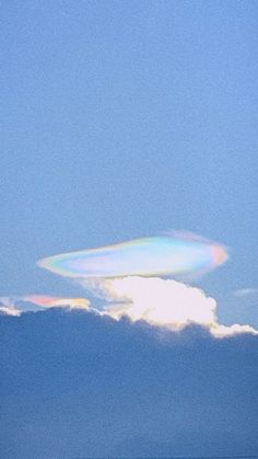 a rainbow colored object is in the sky above water and clouds on a sunny day