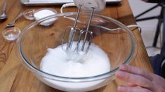 someone mixing ingredients in a glass bowl on a wooden table with an electric blender