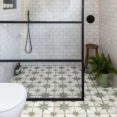 a bathroom with white tiles and green plants in the corner, along with a black framed shower door