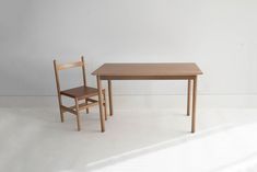 a small wooden table and chair sitting next to each other on a white floor in front of a wall