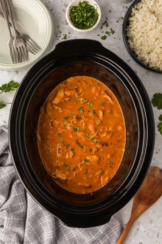 an overhead view of a stew in a crock pot with rice and garnishes