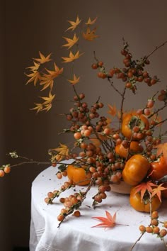 a table topped with lots of oranges and other autumn decorations on top of a white table cloth